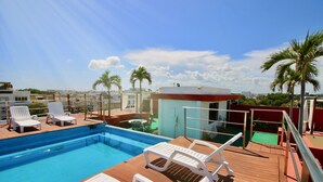 A rooftop pool with white lounge chairs, a small poolside bar, and palm trees in the background. - Praia Apartments by Casago (Playa del Carmen)