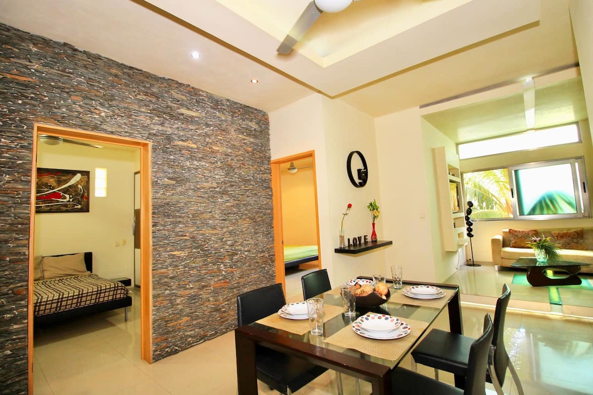 A modern dining area with a glass table, black chairs, and a stone accent wall.