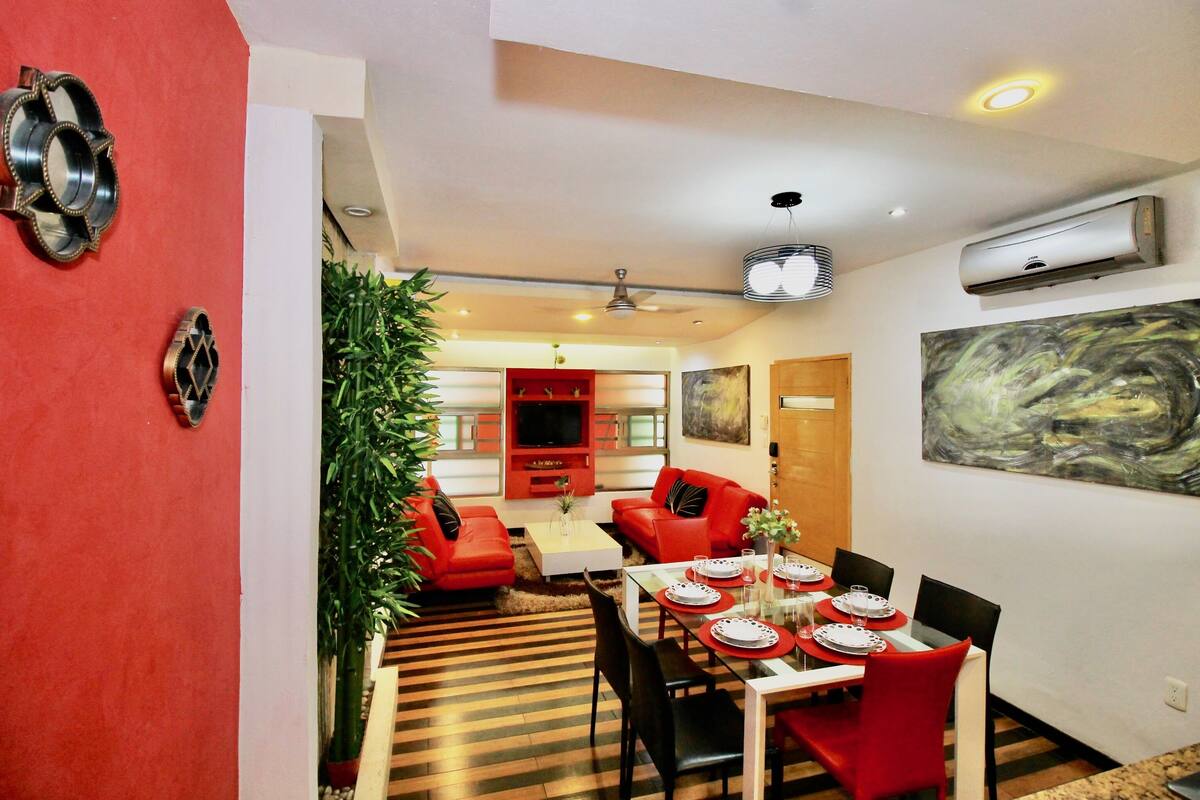 A dining area with a red and black color scheme, a modern ceiling fan, and a large abstract painting on the wall.