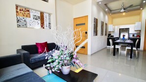 A modern living room with a sofa, a coffee table with a floral arrangement, and a dining area with a kitchen in the background. - Praia Apartments by Casago (Playa del Carmen)