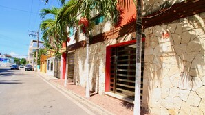 A street view with a building featuring stone walls, red shutters, and a visible number '10'. - Praia Apartments by Casago (Playa del Carmen)