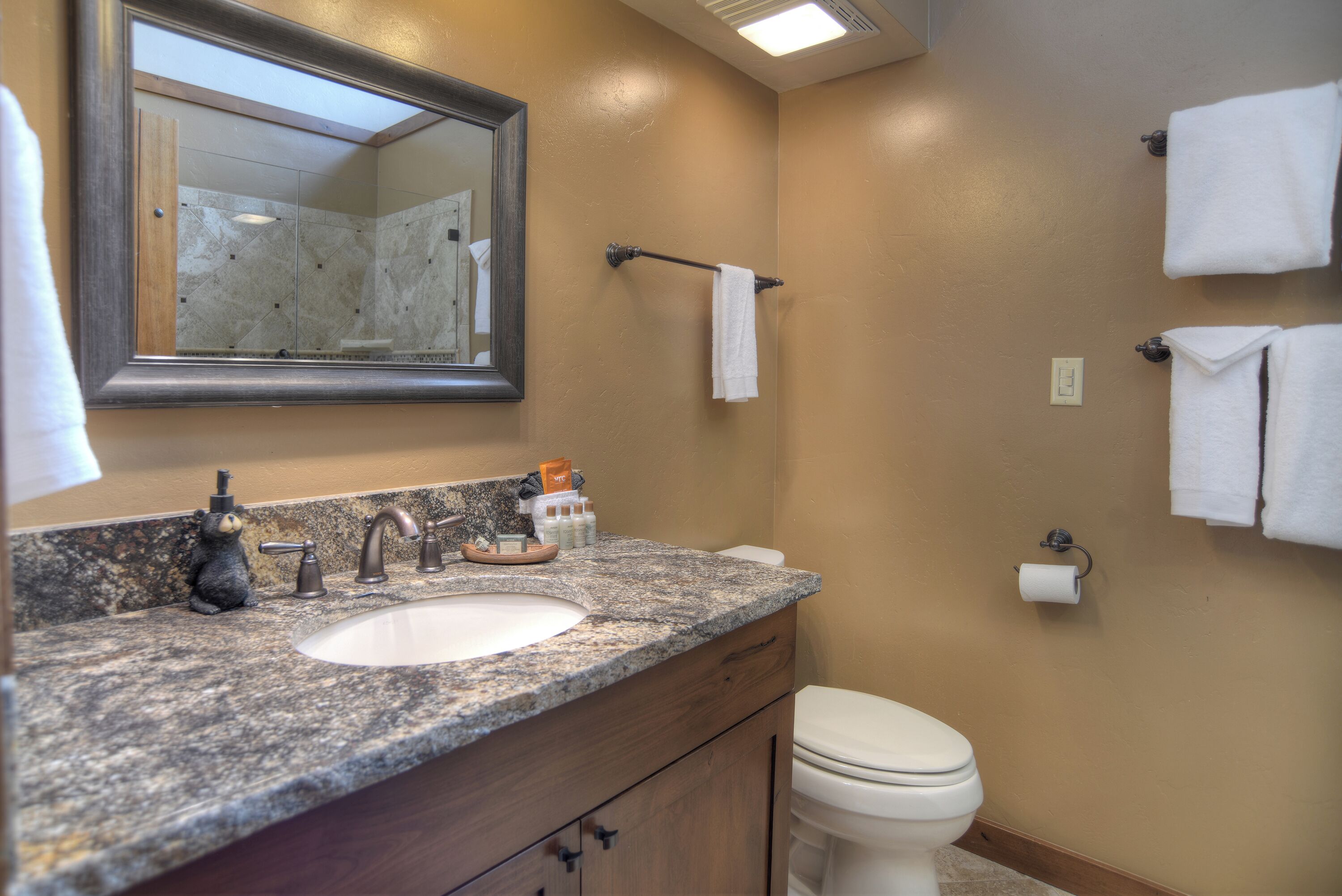 A bathroom with a granite countertop, a sink, a mirror, a toilet, and a towel rack.
