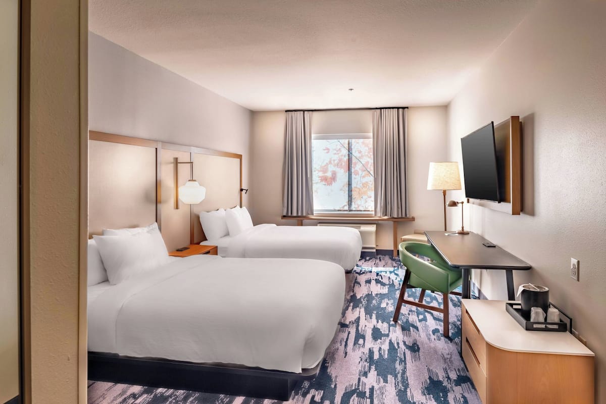 Une chambre d’hôtel avec deux lits, un bureau avec une chaise, une télévision et une fenêtre avec des rideaux.