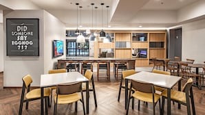 Un espace repas moderne avec des tables et des chaises en bois, des luminaires suspendus et un grand écran diffusant une vidéo.