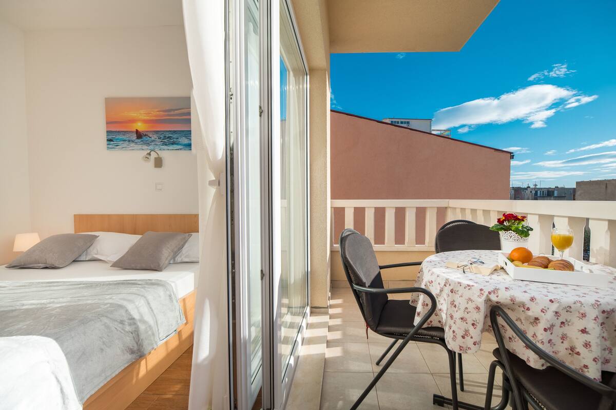 A balcony with a bed, a table with breakfast, and a sunset painting.