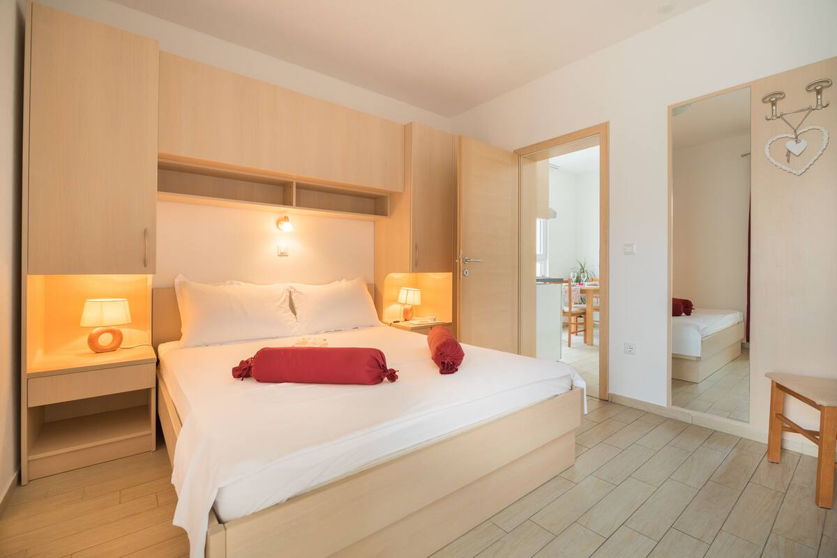 A hotel room with a large bed, two bedside tables with lamps, a wooden headboard, and a mirror on the wall.