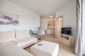 A modern living room with a sofa, a coffee table, and a TV stand. There is a dining area with a table and chairs, and a kitchen in the background. - Villa Lelas (Makarska)