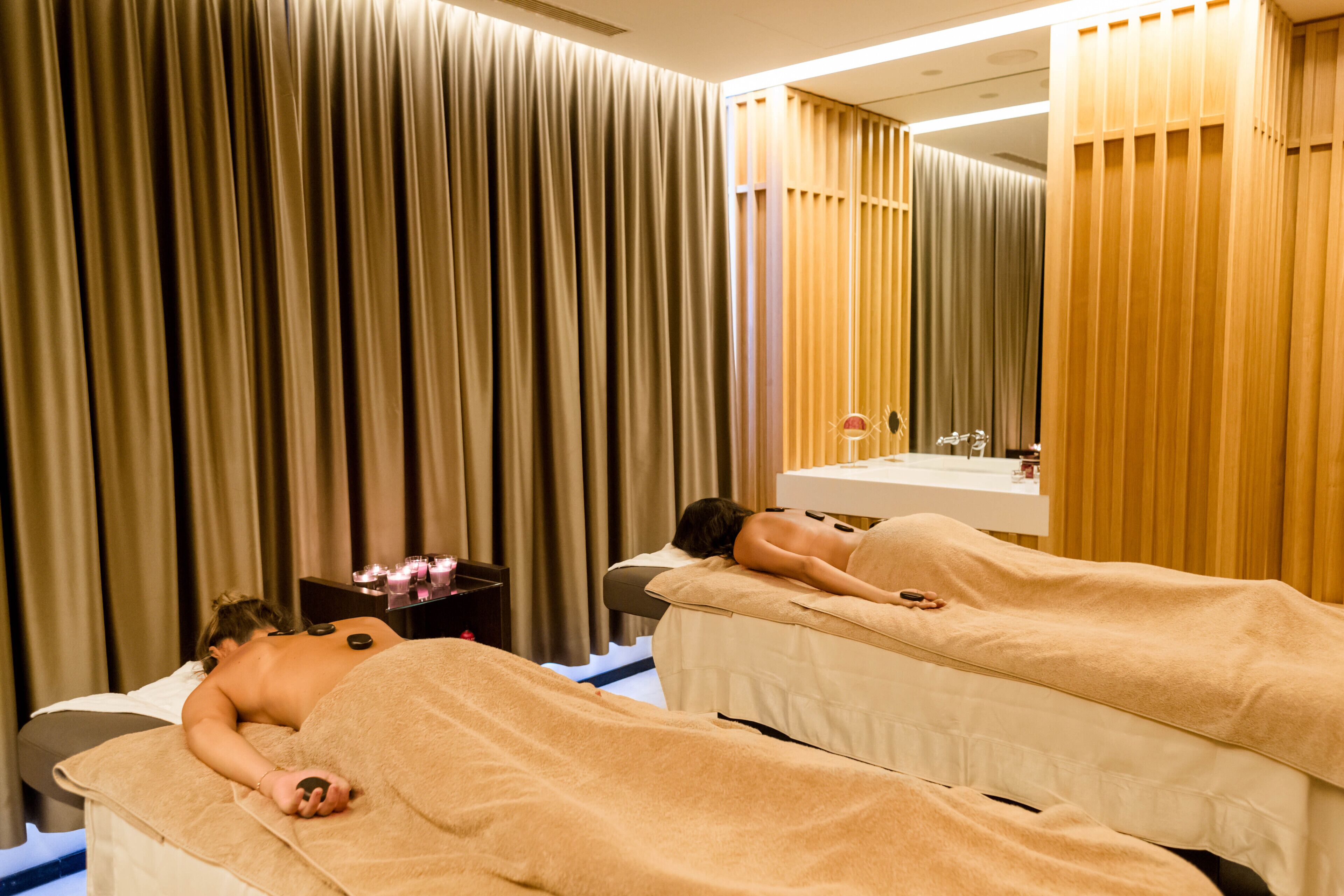 Un cuarto de spa con dos camillas de masaje, un espejo y un lavamanos.