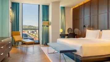 Een hotelkamer met een groot bed, een bureau, een stoel en uitzicht op een stadsbeeld door grote ramen.