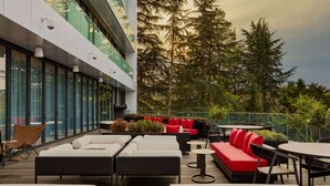Une terrasse sur le toit, dotée d’un espace extérieur aménagé avec des canapés et des fauteuils, entourée de murs en verre et offrant une vue sur les arbres.