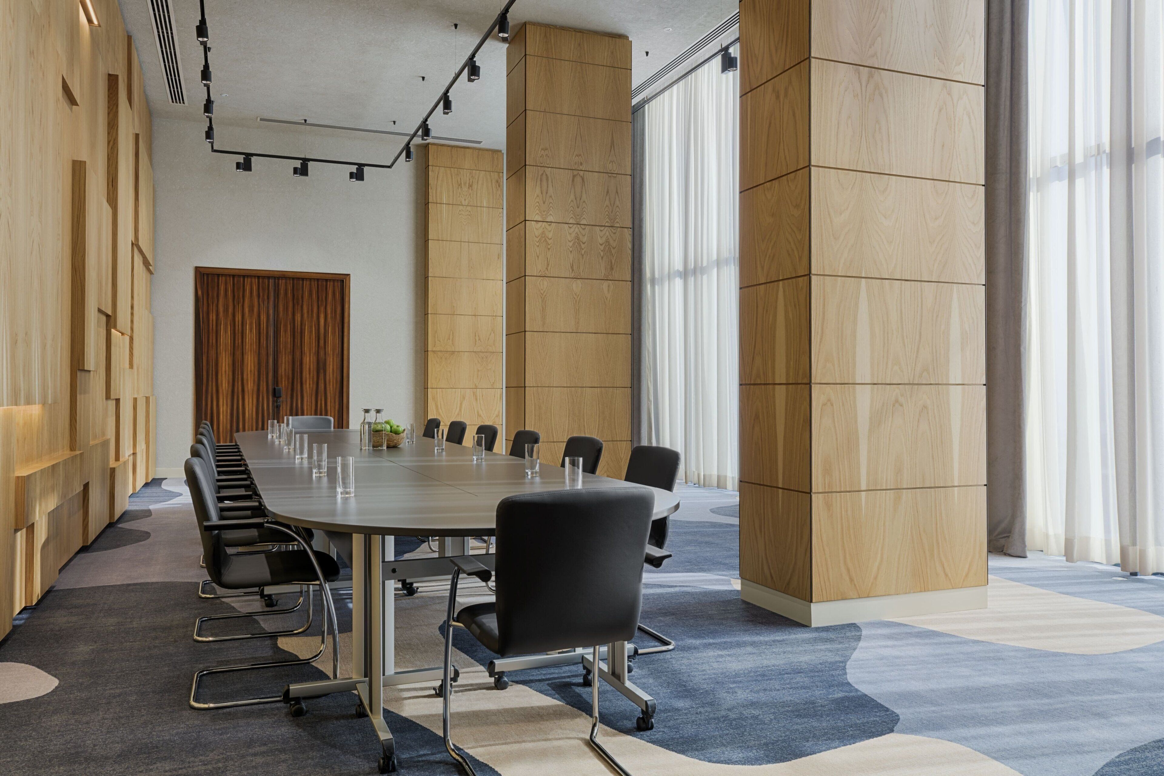 Une salle de conférence avec une longue table, des chaises noires et un mur décoratif en bois.