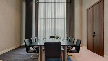 Una sala conferenze con un lungo tavolo, sedie, un'ampia finestra con tende e una porta.