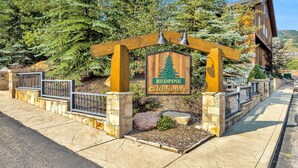 A wooden sign with a pine tree and the words "Redpine Clubhouse" in front of a building with stone walls and a wooden deck.