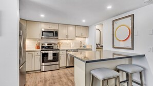 A modern kitchen with stainless steel appliances, a central island with stools, and light-colored cabinetry.