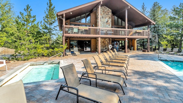 A two-story building with a stone facade, a balcony with outdoor seating, and a swimming pool area with lounge chairs.