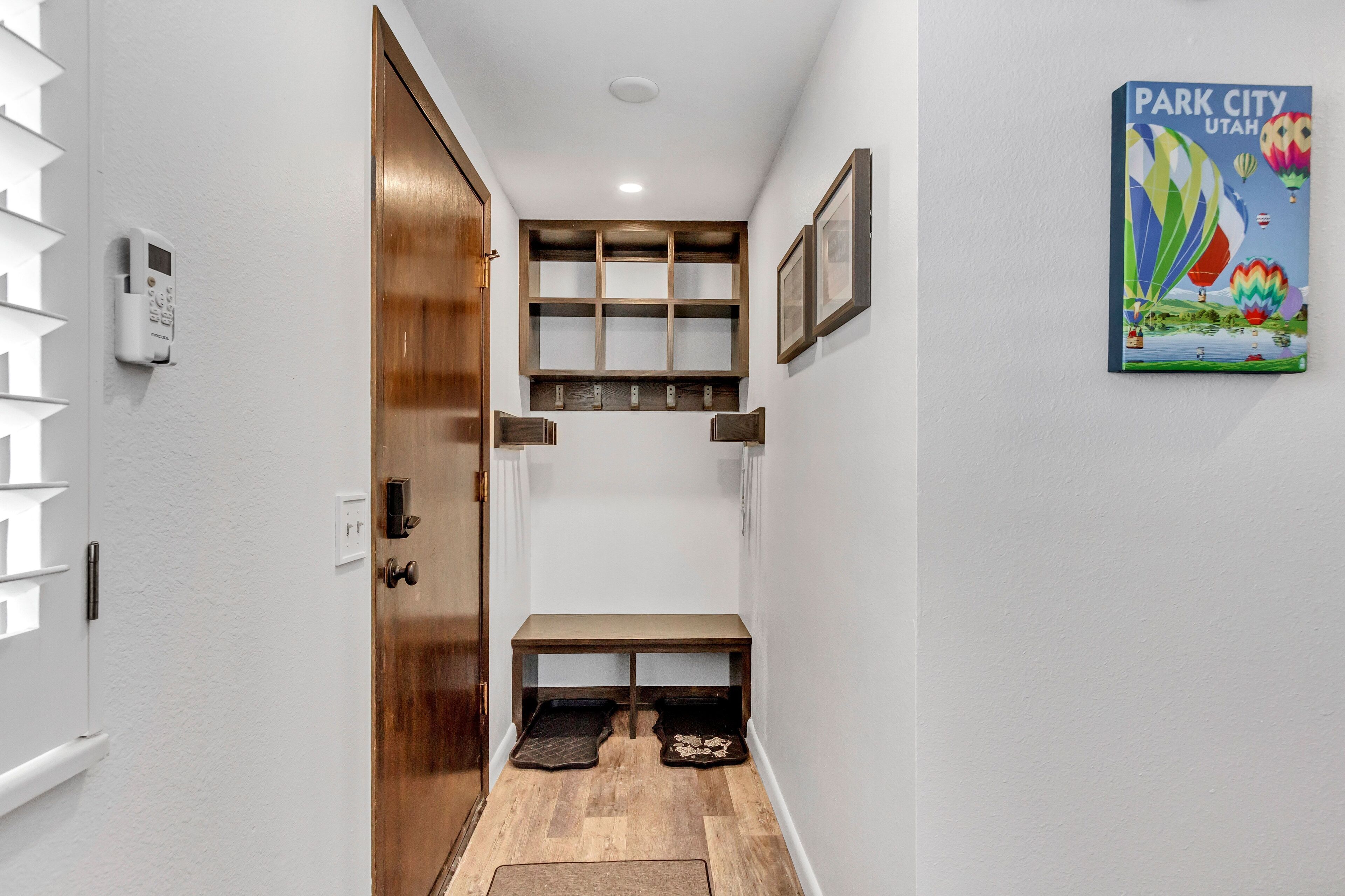 A hallway with a wooden door, a wall-mounted security system, a bench, and a framed picture of Park City, Utah.