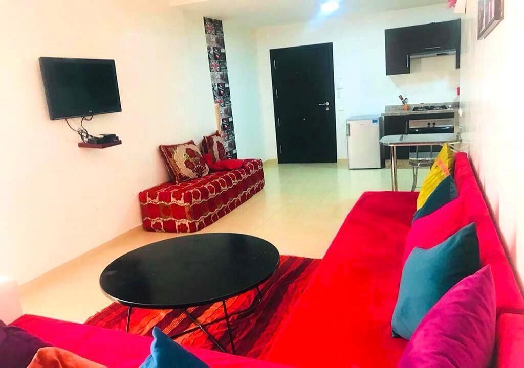 Ein Wohnzimmer mit einem roten Sofa, einem schwarzen Couchtisch und einem an der Wand befestigten Flachbildfernseher.