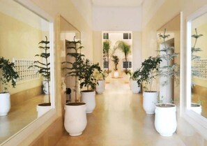 A hallway with potted plants on either side and a view of a courtyard through an open door. - Superb Studio Residence Rita Marrakech 4625 (Marrakech)