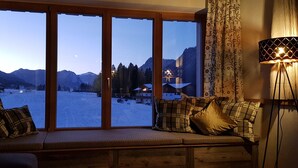 Une pièce chaleureuse avec une grande fenêtre donnant sur un paysage enneigé et des montagnes.