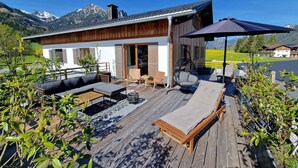 Une terrasse en bois avec des sièges d’extérieur, un fauteuil suspendu et un espace abrité comprenant une table et des chaises.