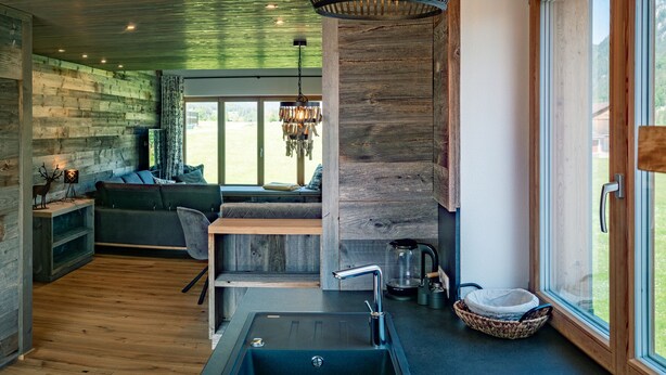 Un intérieur moderne avec un escalier en bois, un coin salon confortable, une cuisine équipée d’un évier et une vue sur l’extérieur.