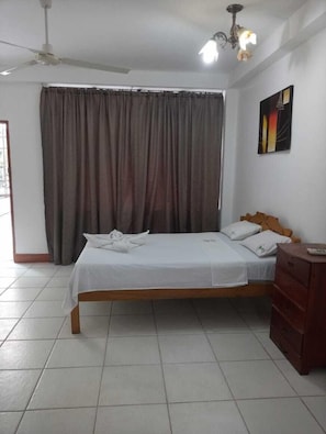 A bedroom with a bed, curtains, a ceiling fan, a chandelier, a dresser, and a painting on the wall.