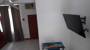A room with a ceiling fan, a desk with a chair, a TV mounted on the wall, and a red door. - Gran hotel Jungla (Iquitos)