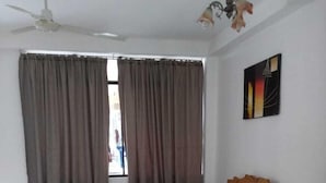 A bedroom with a bed, curtains, a ceiling fan, a nightstand, and a painting on the wall. - Gran hotel Jungla (Iquitos)