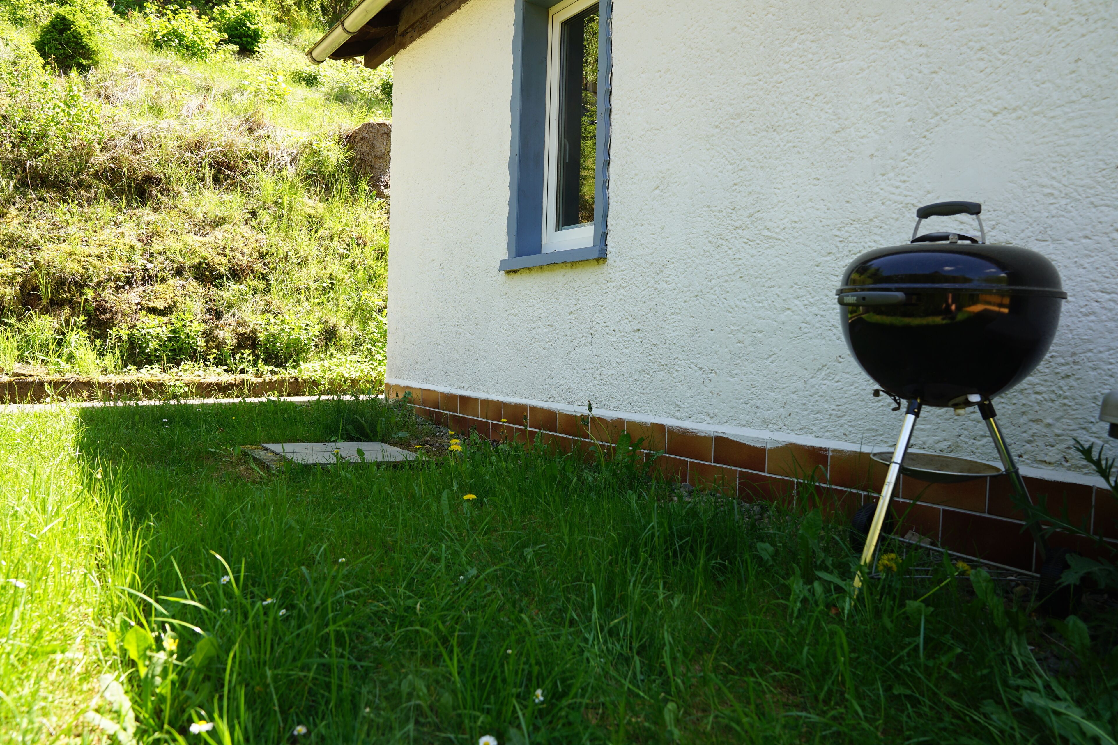 Een huis met een raam en een zwarte barbecue in de voortuin.
