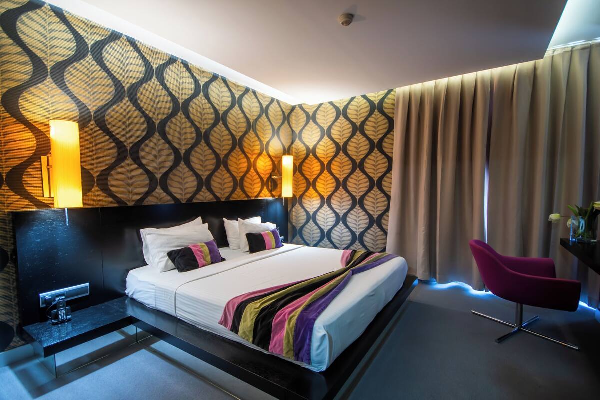 A modern hotel room with a large bed, a desk, a chair, and a patterned wall.