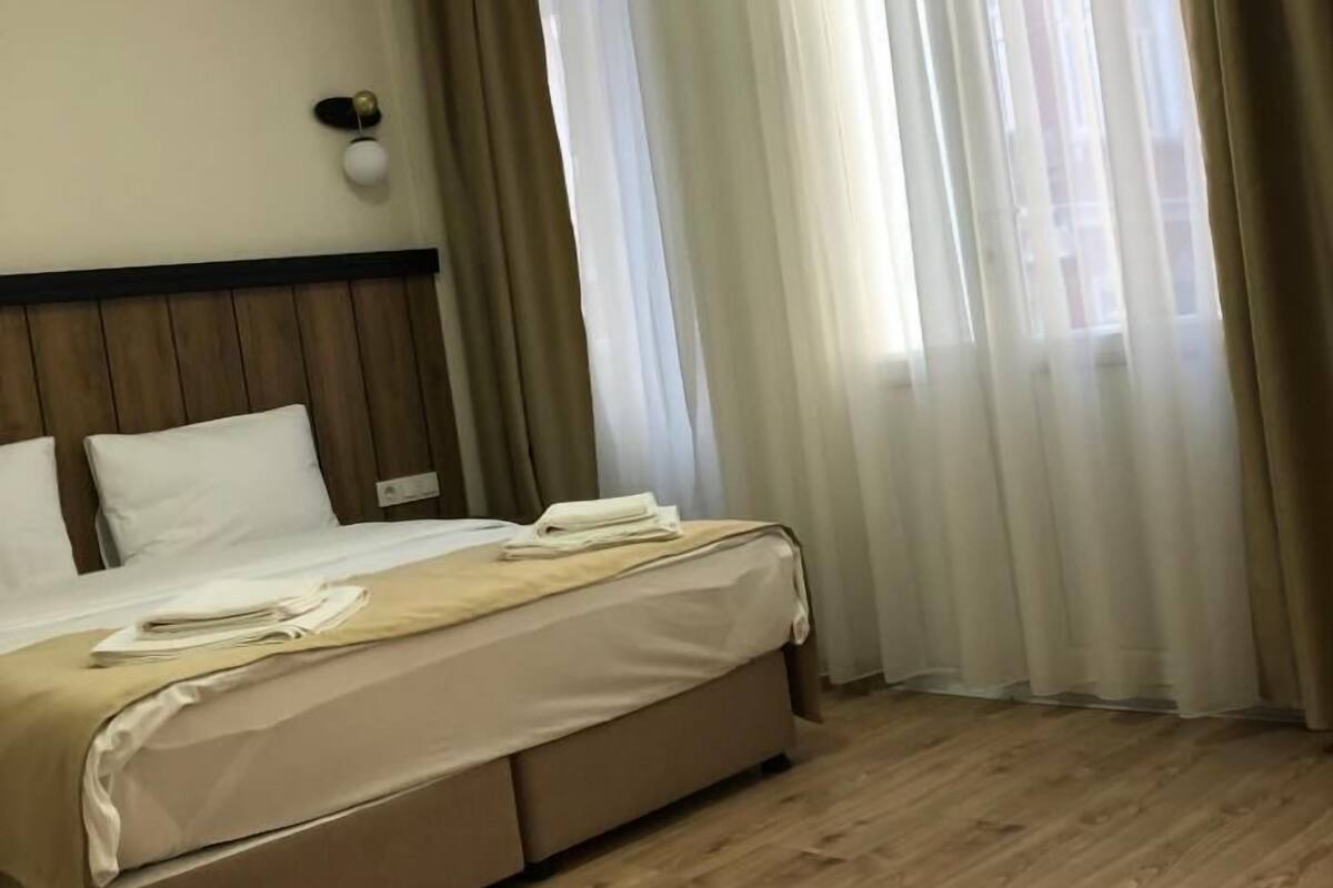 A hotel room with a bed, wooden flooring, and sheer curtains.