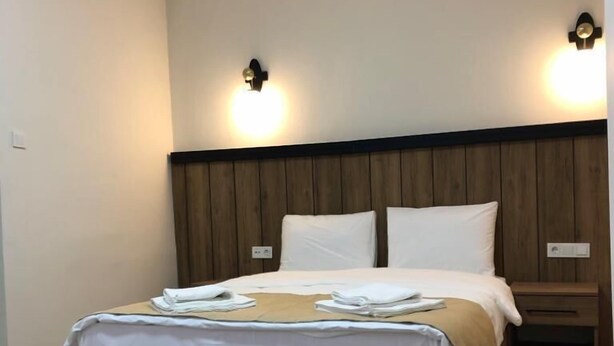 Ein Hotelzimmer mit einem hölzernen Kopfteil, einem Bett mit weißen Leinen und zwei Wandleuchten.