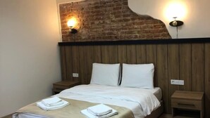Ein ordentlich bezogenes Bett mit weißen Leinen, zwei Nachttische, eine Wand mit Ziegeln und ein Holzboden.