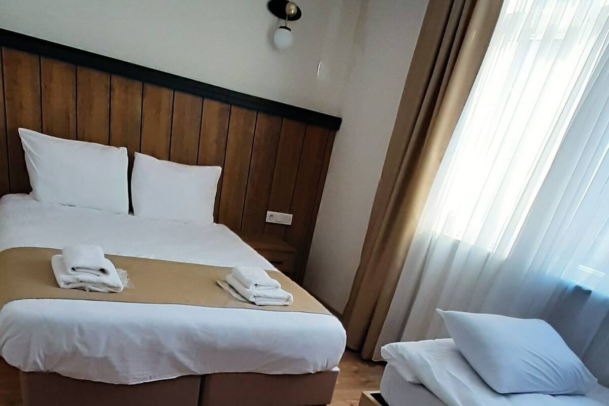 A hotel room with a large bed, a smaller bed, wooden flooring, and a ceiling light fixture.