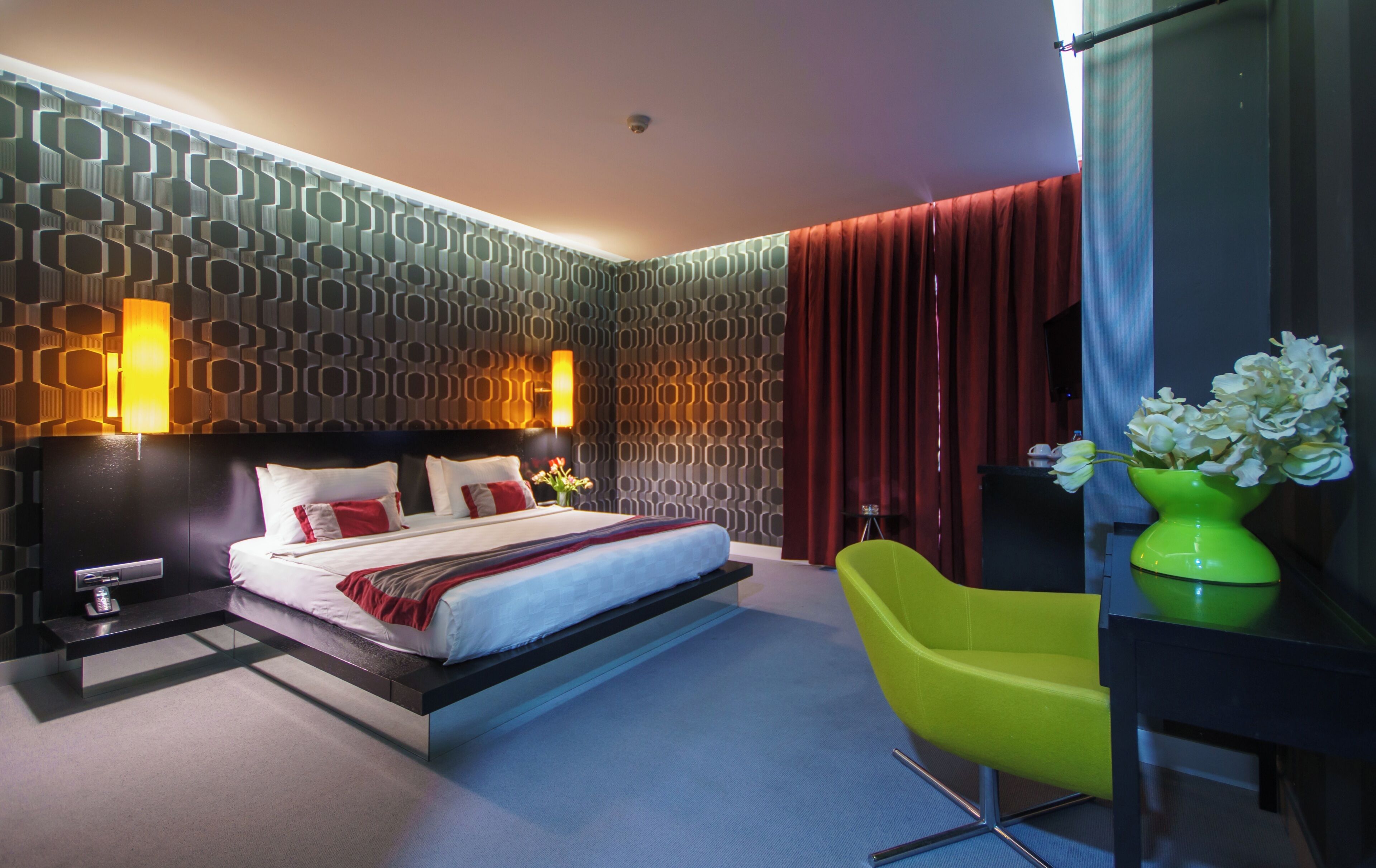 A modern hotel room with a bed, a desk, a chair, and a vase of flowers.