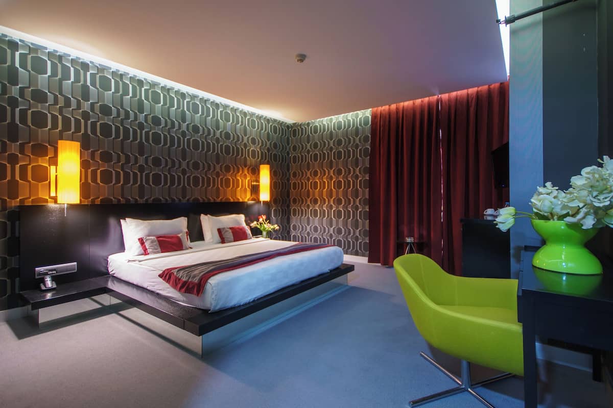 A modern hotel room with a bed, a desk, a chair, and a vase of flowers.
