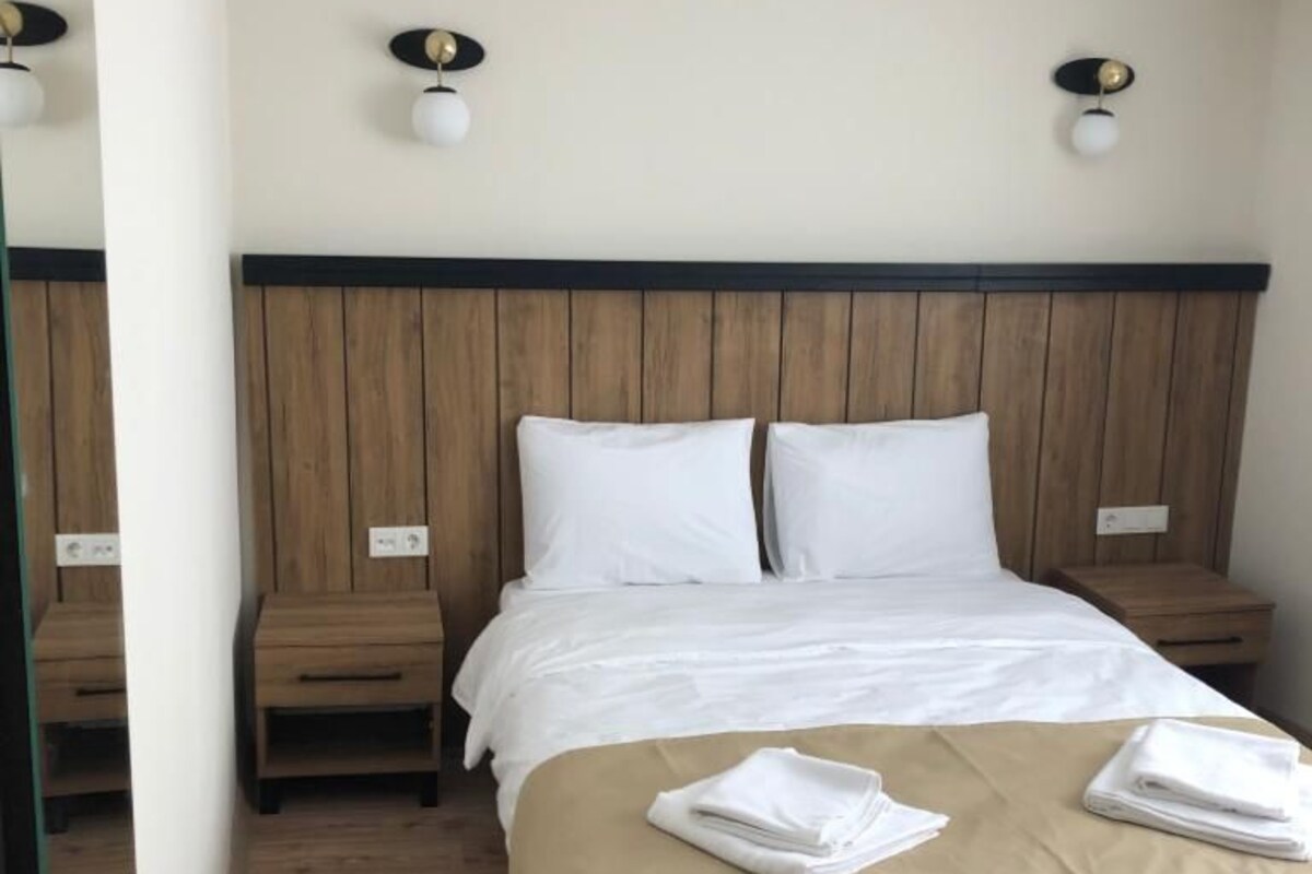 A hotel room with a wooden headboard, a bed with white linens, two bedside tables, and a mirror on the wall.