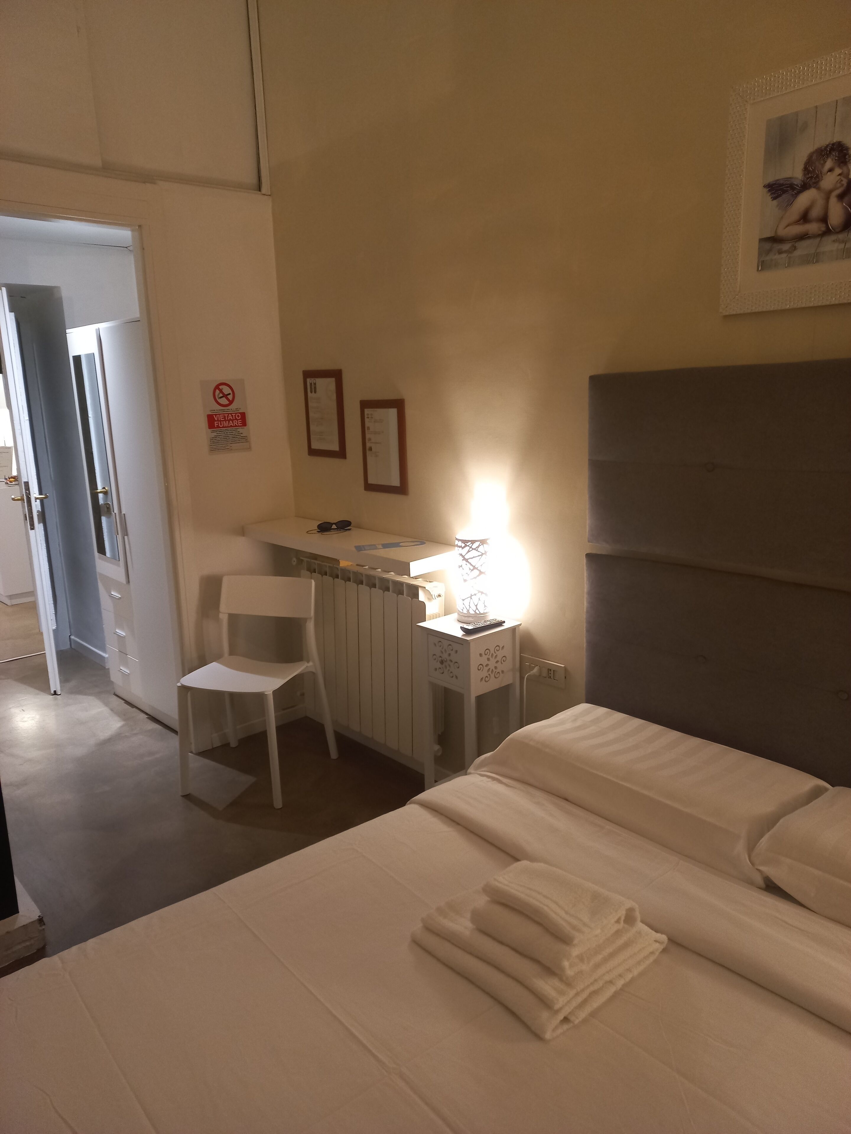 A hotel room with a bed, a desk with a chair, a lamp, and a framed picture on the wall.