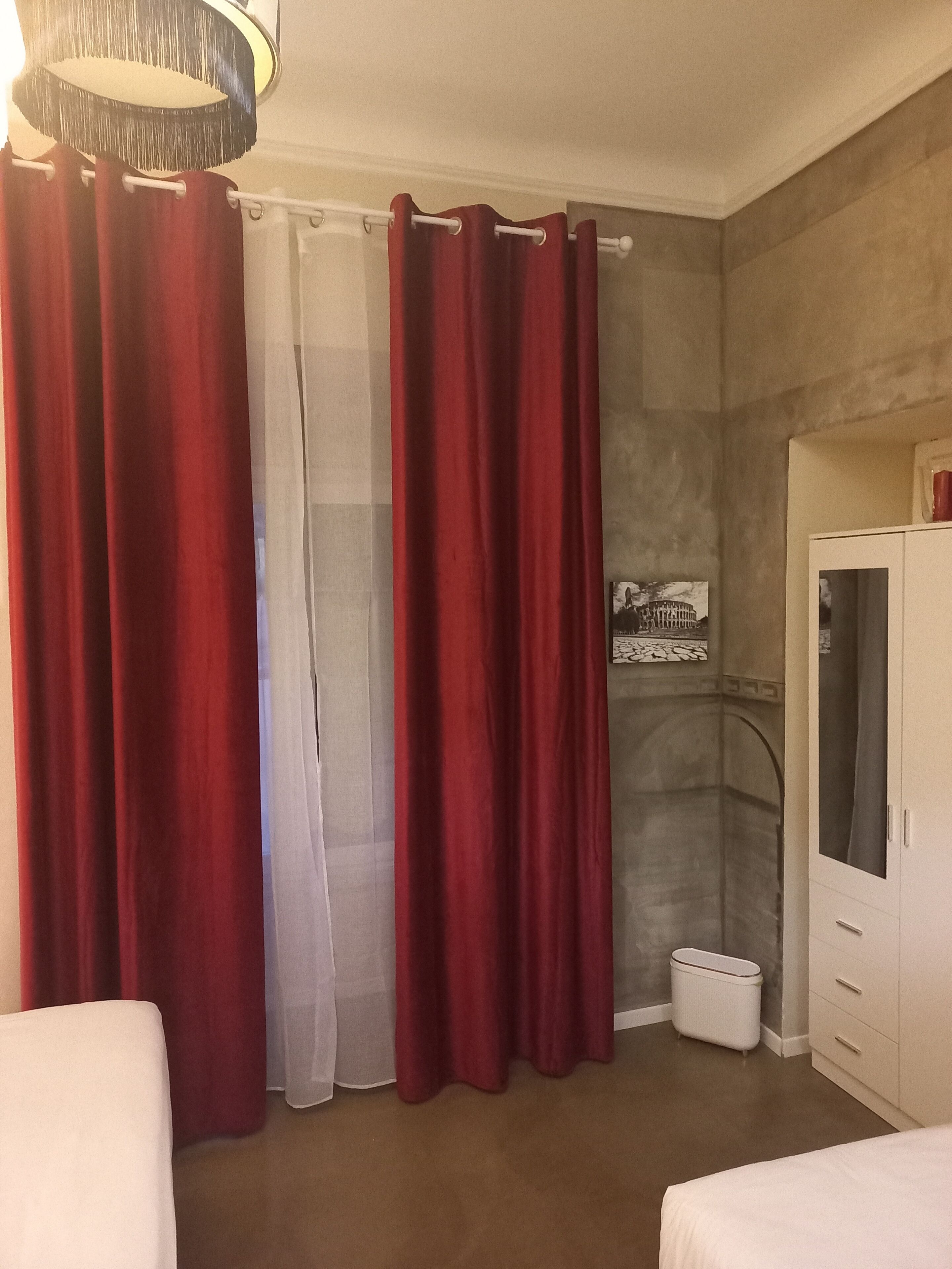 A hotel room with a bed, a wardrobe, a small trash bin, and a shower area.