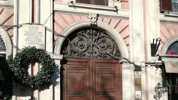 A historic building with ornate architectural details, a large wooden double door, and a sign commemorating a historical event. - Stefano House Roma (Rome)