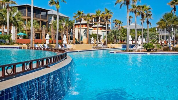 Un resort con una grande piscina, palme e edifici moderni.