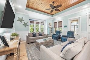 A spacious living room with a ceiling fan, a sofa set, a coffee table, and a TV.