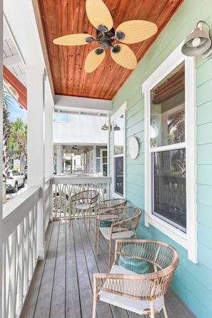 A wooden porch with wicker chairs, a ceiling fan, and a view of the street.
