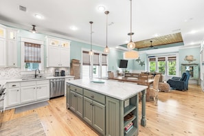 A spacious kitchen with white cabinets, a central island, and pendant lighting.