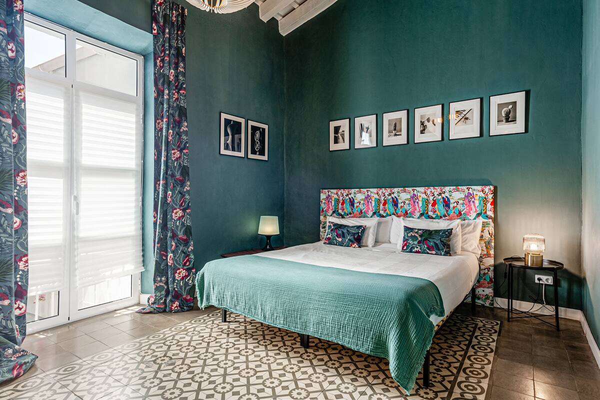 Une chambre à coucher avec un lit, une table de chevet, une lampe et une fenêtre avec des rideaux.
