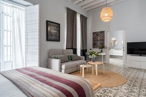 A modern bedroom with a bed, a sofa, a TV, and a dining area with a table and chairs.