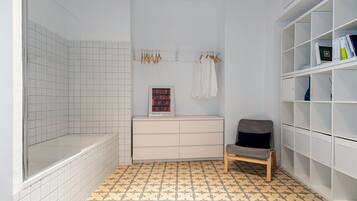 Bathroom features a minimalist design with a tiled floor, a bench, and a shelving unit.