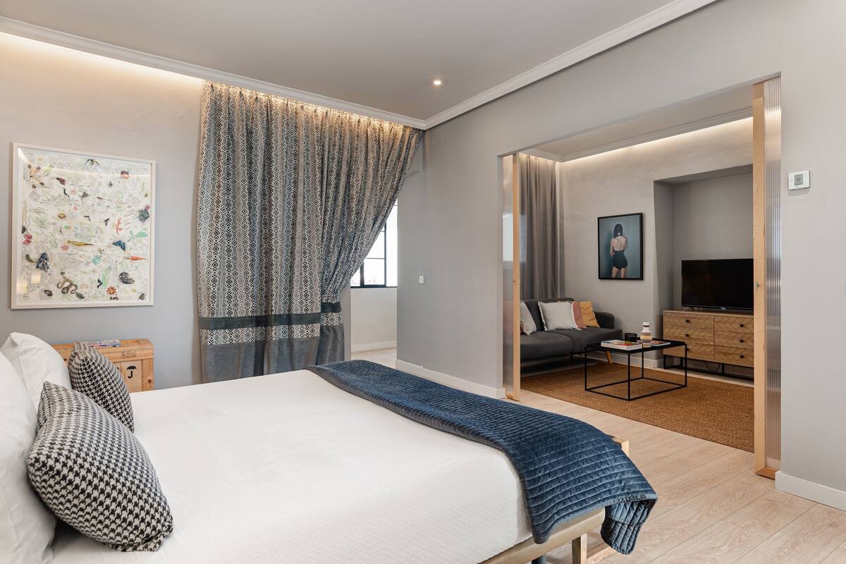 Une chambre moderne avec un grand lit, une table de chevet et une vue sur le salon.