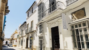 A row of white buildings with black metal bars on windows and doors, a sign reading "CASA DE INDIAS," and a plaque above the door. - Art Suites by Casa de Indias (El Puerto de Santa Maria)