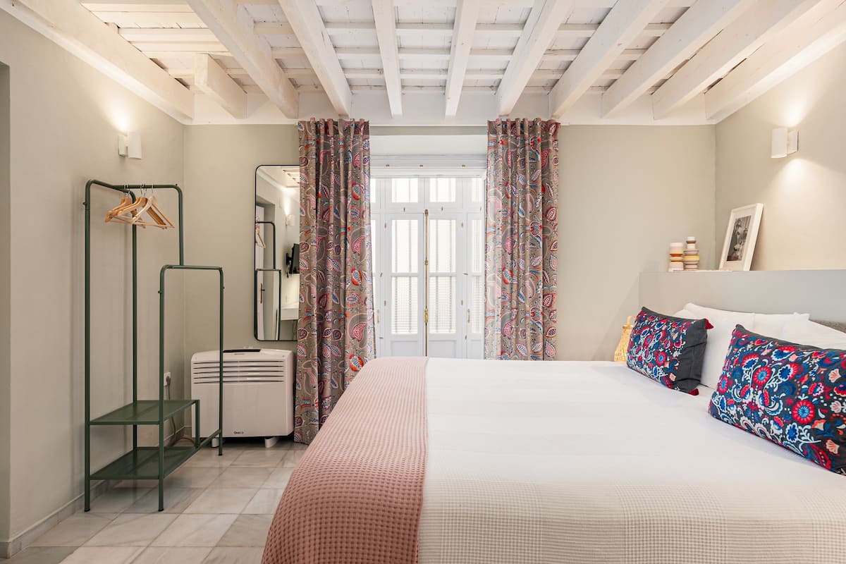 Une chambre à coucher avec un lit, une armoire, un miroir et une porte ornée de rideaux à motifs.
